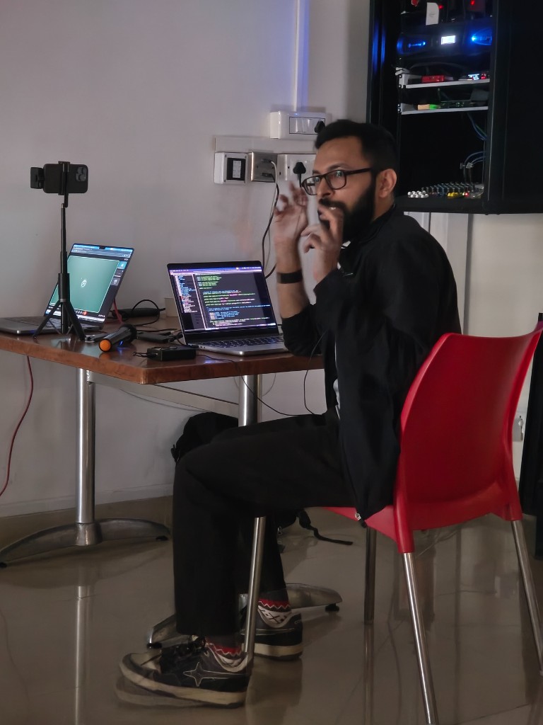 Speaker explaining setup from a side desk with laptops and networking gear visible